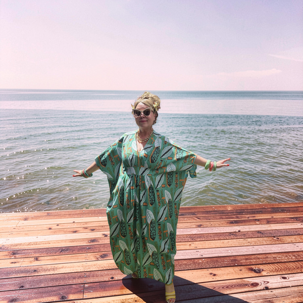Woman in a green patterned dress standing on a wooden dock by the ocean. Spoonflower pablo's lounge tiki caftan seersucker